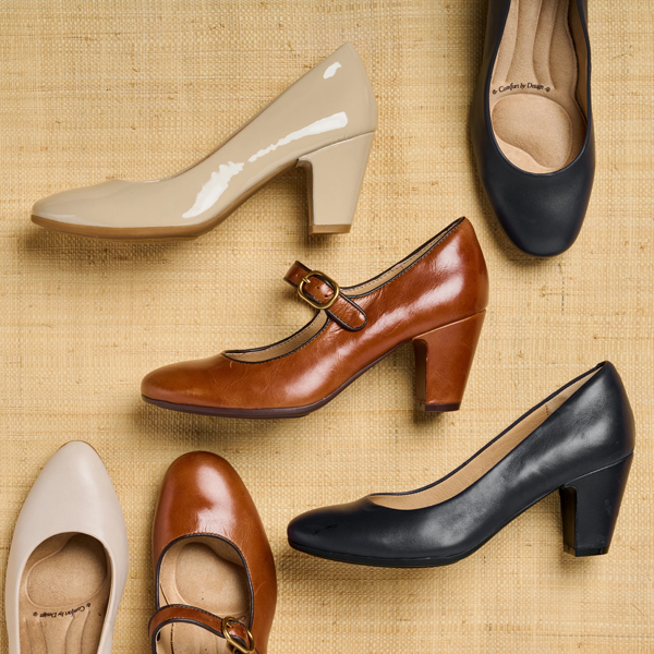 Several pairs of pumps laying on a tan fabric background. Featuring The Lana pump in Tan, Parisa pump in Grey, Leslie pump in tan, and Lana pump in Black. Shop Dress pumps and Pumps.